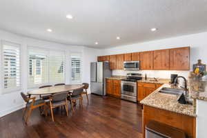Kitchen featuring light stone countertops, recessed lighting, brown cabinetry, stainless steel appliances, and a sink