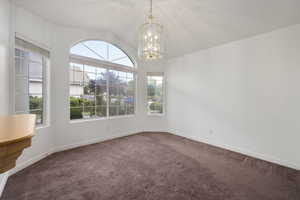Carpeted empty room featuring an inviting chandelier, baseboards, and vaulted ceiling