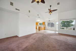 Unfurnished living room featuring ceiling fan, visible vents, high vaulted ceiling, baseboards, and light carpet