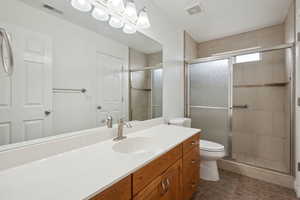 Bathroom featuring toilet, visible vents, a shower stall, and vanity