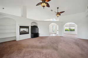 Unfurnished living room featuring high vaulted ceiling, light carpet, a ceiling fan, and arched walkways