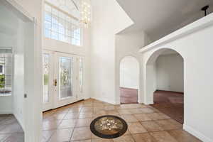 Tiled entrance foyer featuring arched walkways, a high ceiling, a notable chandelier, and baseboards