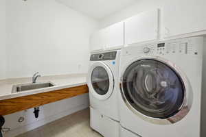 Clothes washing area with washer and dryer, light floors, a sink, and cabinet space