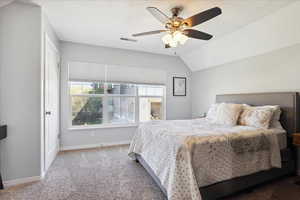 Carpeted bedroom with a ceiling fan, baseboards, visible vents, and vaulted ceiling