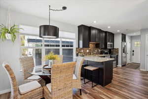 Kitchen with decorative backsplash, dark wood-style floors, light stone counters, a sink, and stainless steel appliances