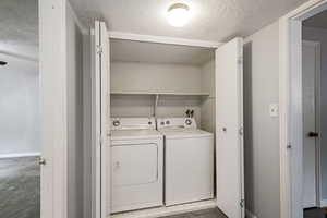 Laundry area featuring carpet flooring, laundry area, a textured ceiling, baseboards, and washer and clothes dryer