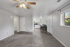 Living room featuring ceiling fan, a textured ceiling, visible vents, baseboards, and dark carpet
