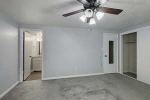 Unfurnished bedroom with carpet floors, a closet, baseboards, ensuite bathroom, and a textured ceiling