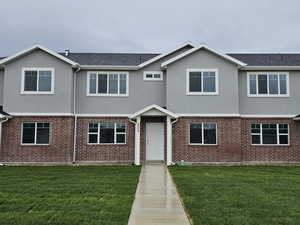 View of front of property with stucco siding, a front lawn, and brick siding