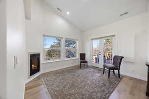 Sitting room featuring high vaulted ceiling, white oak wood flooring, gas fireplace, French doors opening on to a wood deck.