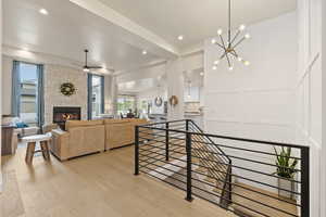 Interior space with recessed lighting, light hardwood floors, a decorative wall, ceiling fan, modern chandelier, stone fireplace, and a stairwell with modern metal railing