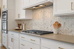 Kitchen featuring stainless steel appliances, tasteful backsplash, custom range hood, quartz countertops, and white cabinets