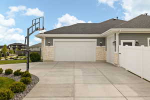 View of property exterior featuring fence, a shingled roof, concrete driveway, and stone siding