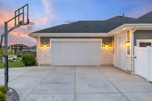 Property exterior at dusk featuring fence with gate, driveway, basketball standard, garage doors, and exterior lighting