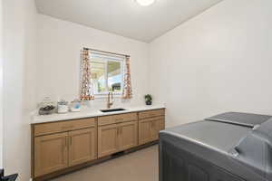 Laundry room with light tile floors, warm wood cabinets, sink, quartz countertops, and separate washer and dryer,