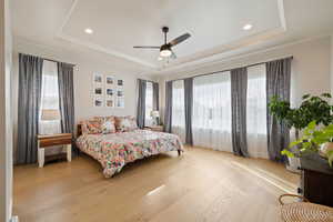 Primary bedroom featuring light hardwood flooring, recessed lighting, ceiling fan, and tray ceiling