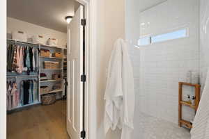 Primary bathroom with a spacious walk-in closet, hardwood floors, and a tiled Roman-style shower