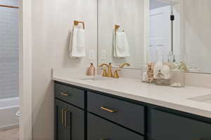 Bathroom featuring double vanity with quartz countertops, two sinks, and gold fixtures
