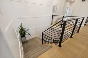 Light hardwood flooring, stairwell with horizontal metal railing, carpeted stairs, and feature wall