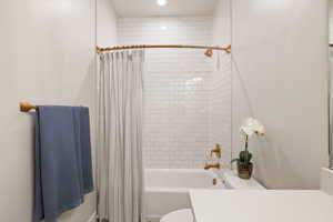 Main floor bathroom with recessed lighting, tiled shower / bath combo with shower curtain, toilet, and vanity with quartz counters