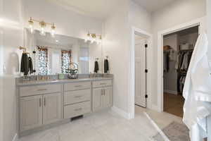 Primary bathroom featuring double vanity, quartz countertops, gold fixtures, tile flooring and a walk in closet