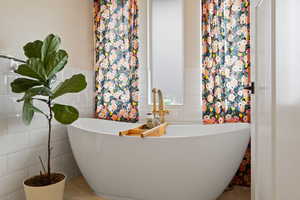 Primary bathroom with wainscot tile walls, a freestanding soaking tub, gold fixtures and multiple windows