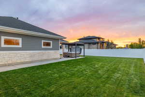 Backyard at dusk featuring a hot tub, pergola, cement sidewalk, vinyl fence, and yard