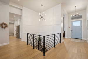 Entryway featuring light hardwood floors, a modern chandelier, and decorative stairwell wall with horizontal metal railing