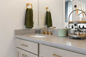Bathroom vanity with quartz countertops, sink, and gold faucet