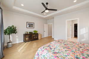 Primary bedroom with a tray ceiling, and light hardwood floors, recessed lighting, ceiling fan, and ensuite bathroom