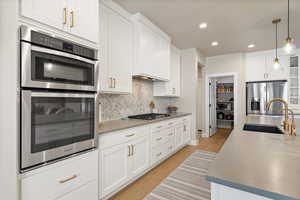 Kitchen featuring a sink, light hardwood flooring, decorative backsplash, white cabinets, and stainless steel appliances