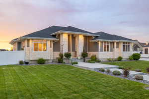 Prairie-style house with a professionally landscaped front yard, covered porch, exterior lighting, mixed finishes of cement-fiber siding and light colored stone, with vinyl fence