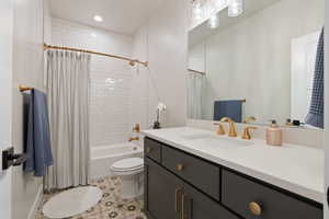 Full main floor bathroom with tiled shower / bath combination, toilet, single vanity with quartz countertops, tile flooring, and gold fixtures