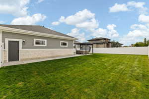 Rear view of property with a lawn, stone siding, a hot tub, and fence