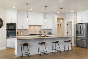 Kitchen featuring white cabinets, stainless steel appliances, decorative backsplash, island with sink, quartz countertops, and pendant lighting