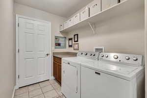 Clothes washing area with separate washer and dryer, baseboards, cabinet space, and light tile patterned floors