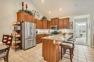 Kitchen featuring brown cabinetry, a peninsula, a sink, light tile patterned floors, and stainless steel appliances