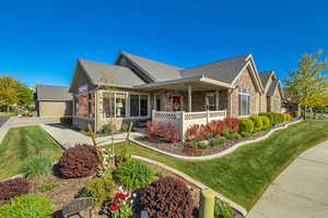 View of front of house featuring a porch, a shingled roof, stone siding, and a front lawn