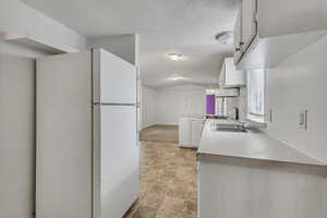 Kitchen featuring stone finish floor, vaulted ceiling, a sink, white cabinets, and freestanding refrigerator