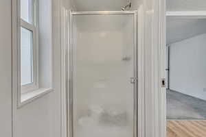 Full bathroom featuring baseboards, a stall shower, a textured ceiling, and wood finished floors