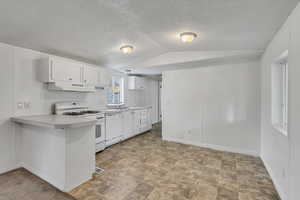 Kitchen featuring lofted ceiling, white appliances, light countertops, white cabinetry, and under cabinet range hood