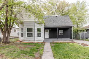View of front of home with fence, a porch, a shingled roof, and a front lawn