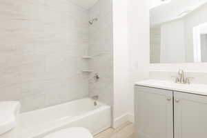 Full bath with shower / bath combination, wood finished floors, vanity, baseboards, and toilet