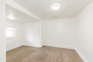 Empty room featuring a textured ceiling, visible vents, light carpet, and baseboards