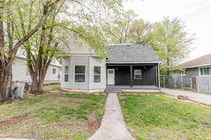 View of front facade featuring fence, roof with shingles, a porch, and a front lawn
