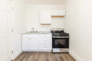 Kitchen featuring stainless steel gas range, a sink, white cabinetry, baseboards, and wood finished floors