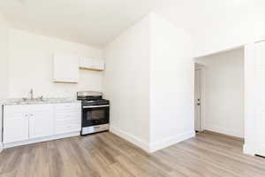 Kitchen with white cabinets, a sink, gas stove, light wood-style floors, and baseboards