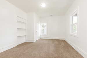 Carpeted empty room featuring baseboards, visible vents, and built in shelves