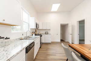 Kitchen with light stone counters, appliances with stainless steel finishes, white cabinets, a sink, and light wood-type flooring