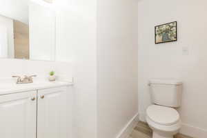 Half bathroom featuring toilet, wood finished floors, vanity, and baseboards